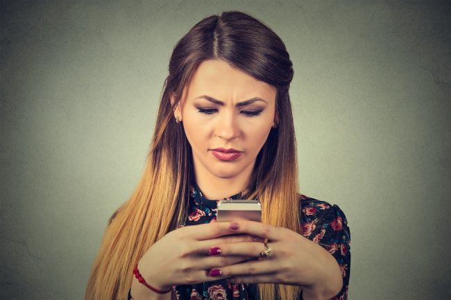 An unhappy woman looking at a smartphone.