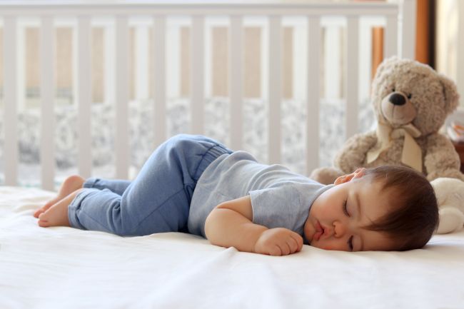 Baby sleeping in crib with teddy bear