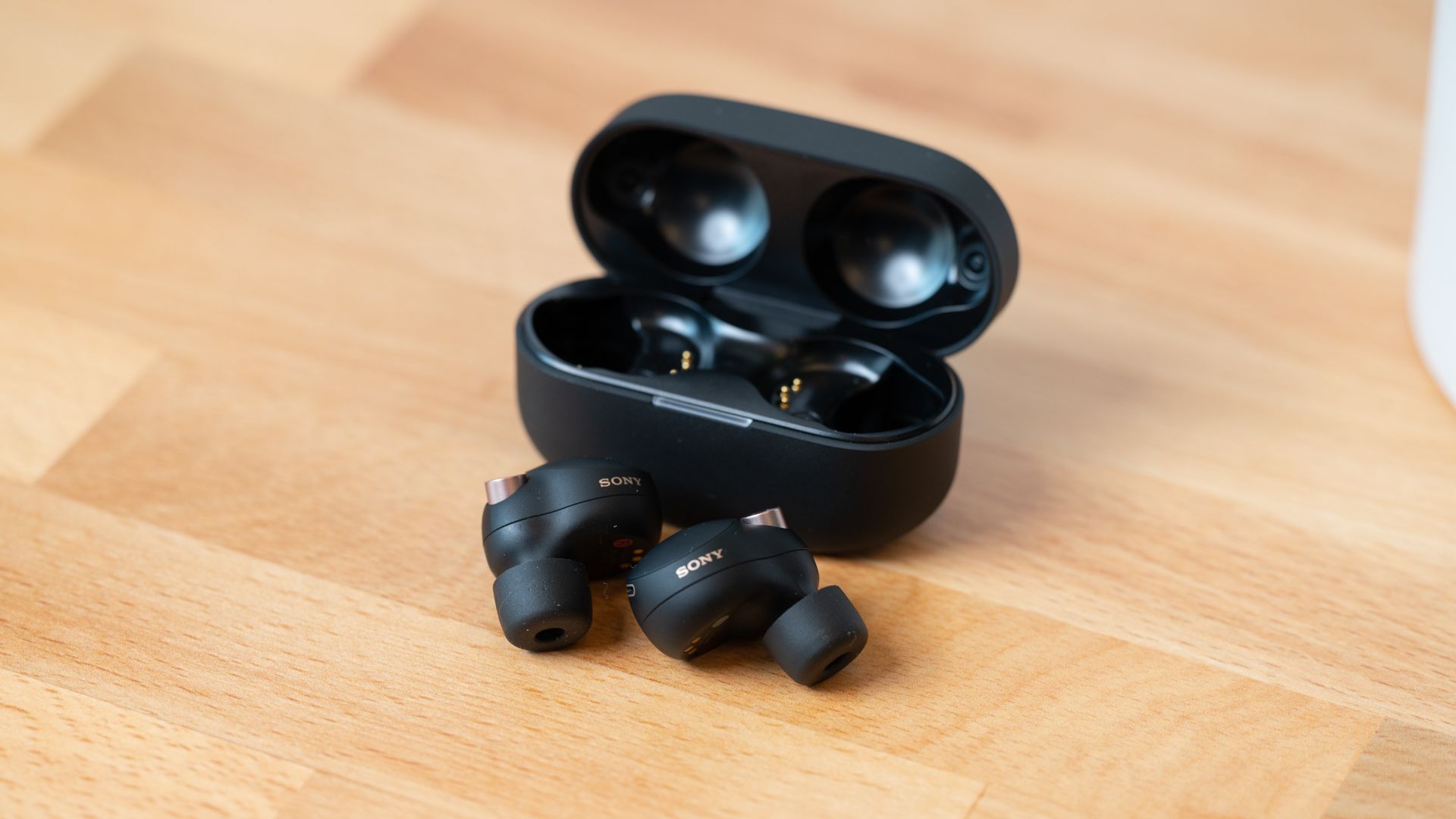 The Sony WF-1000XM4 earbuds and case on a wood table