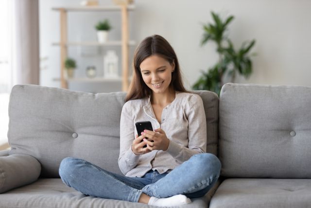 Teenage girl smiling and sitting on couch with smartphone
