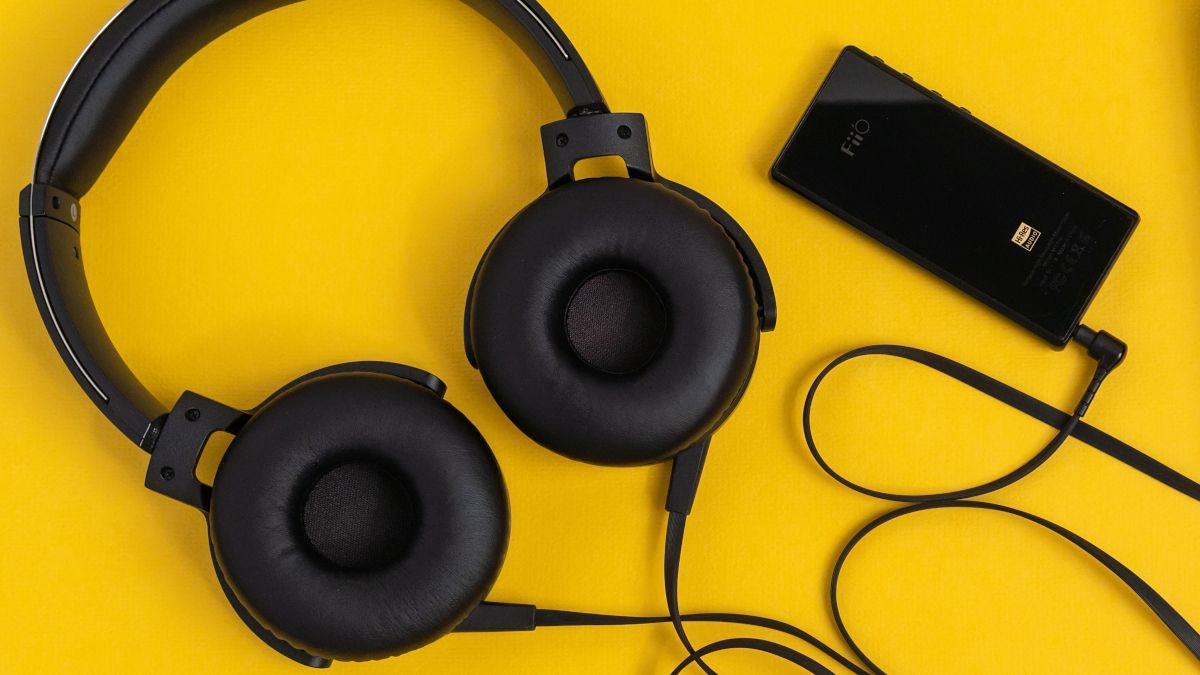 Black wired headphones and audio player on a yellow surface