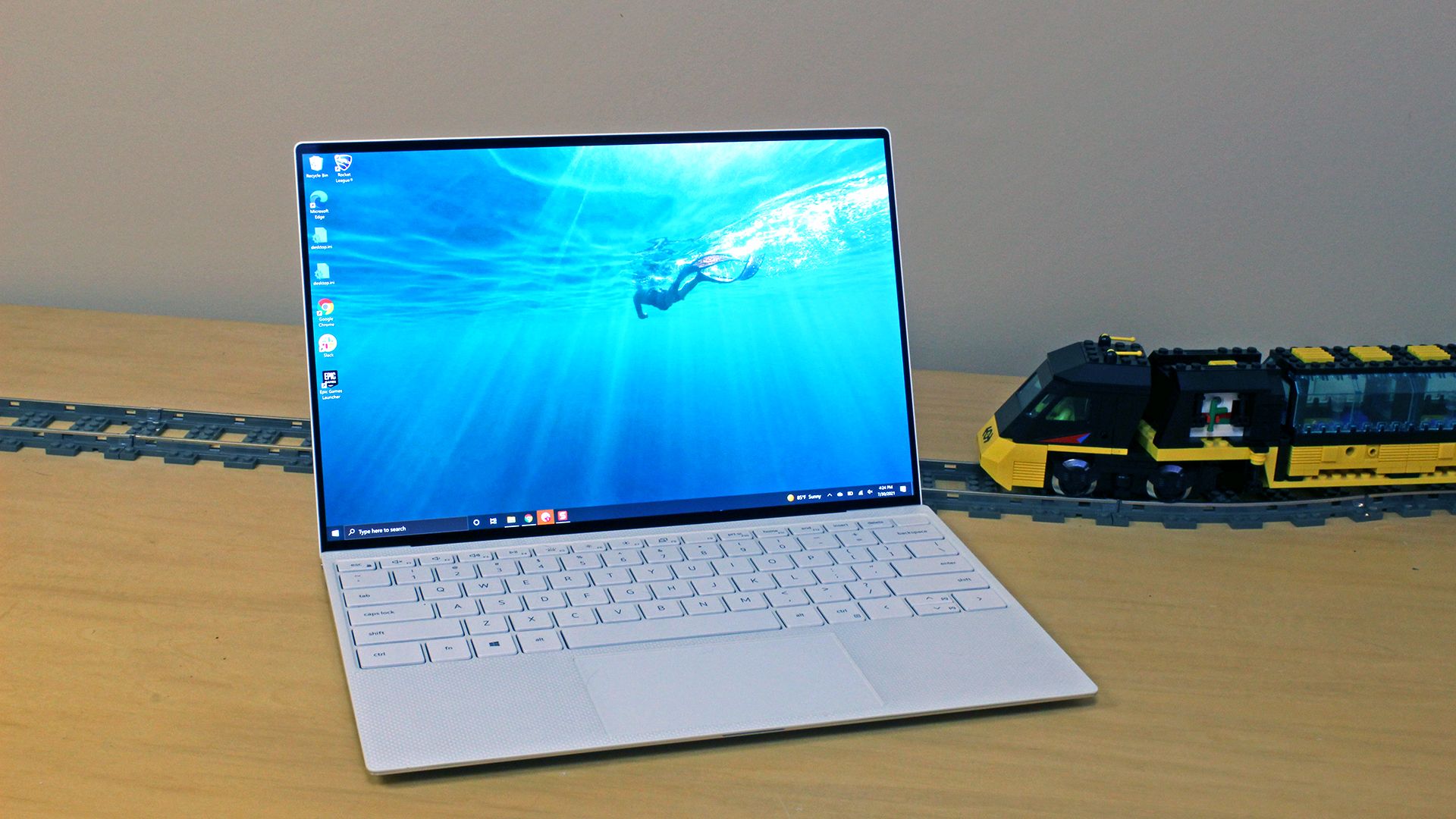 The XPS 13 OLED laptop sitting on a table with a toy train on a traintrack behind it.