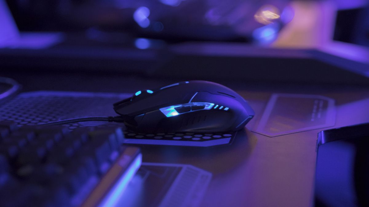 Lit up gaming mouse on computer desk in blue light