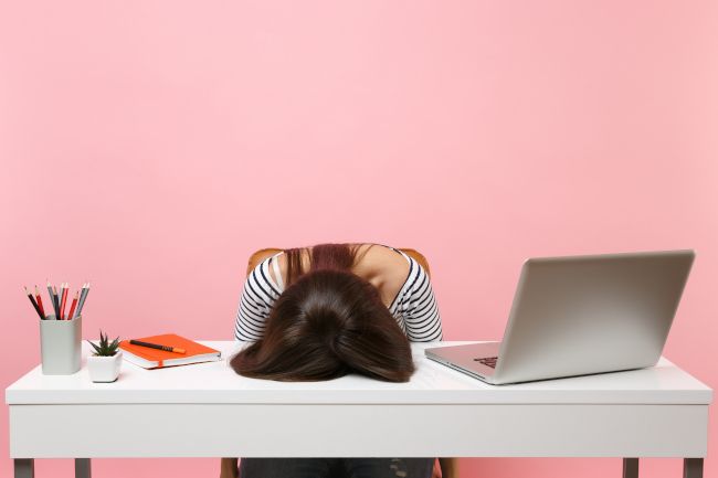 Exhausted woman with face planted on desk next to computer and office supplies.