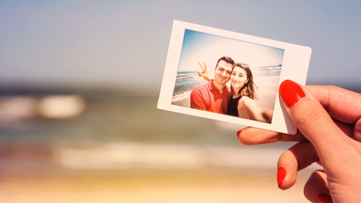 Woman's hand holding photograph of couple in front of beach