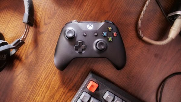 Xbox One controller with headset and keyboard on wood surface.