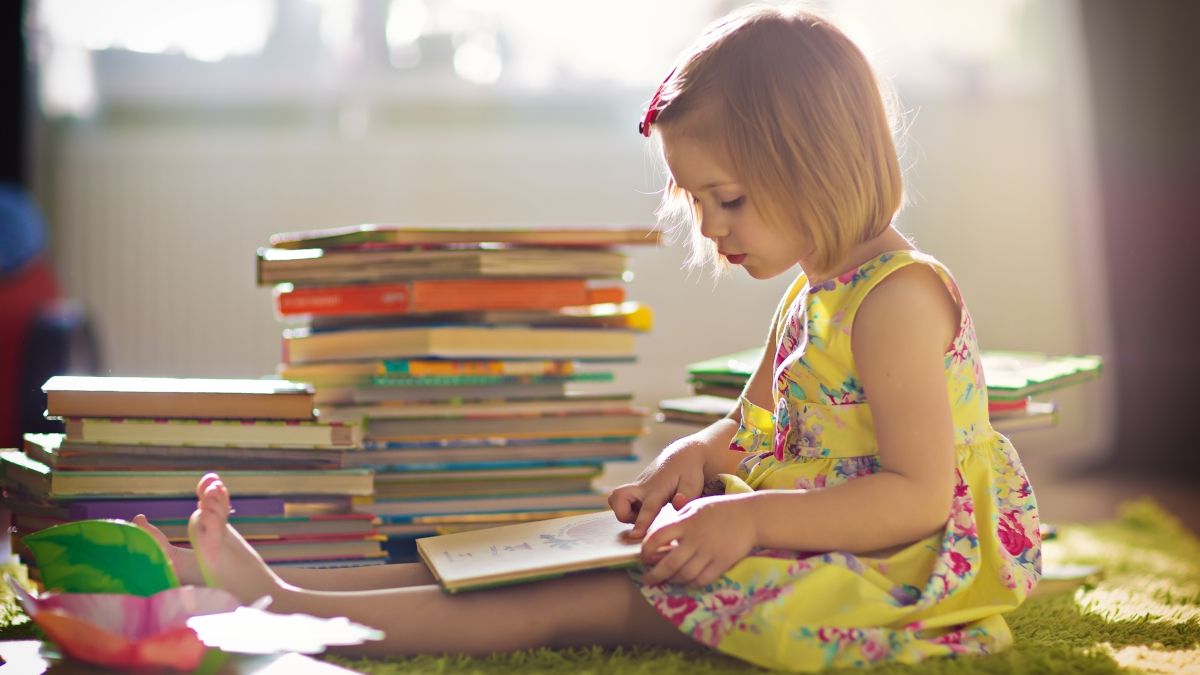 Young girl reading a book in front of a large stack of books