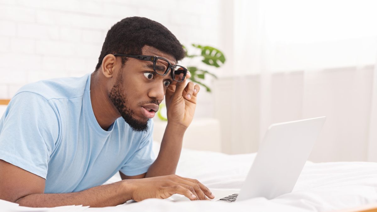 Man lifting glasses and looking shocked at a laptop screen