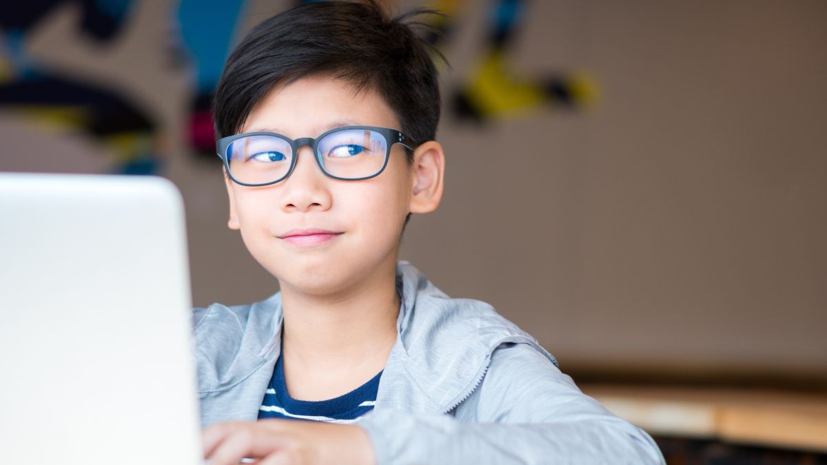 Preteen boy in glasses on a laptop smiling and rolling eyes