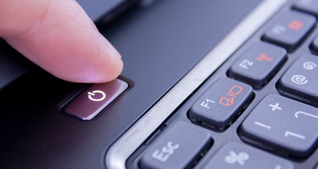 A finger pushing a laptop power button.