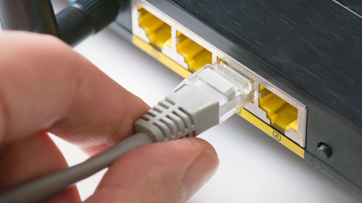 Closeup of a human hand connecting an ethernet cable to a router