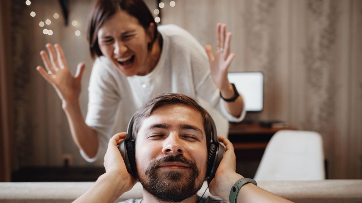 Man wearing headphones with a smile while a woman screams with anger.