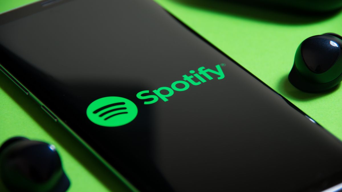Smartphone showing Spotify logo next to wireless earbuds on a green backdrop.