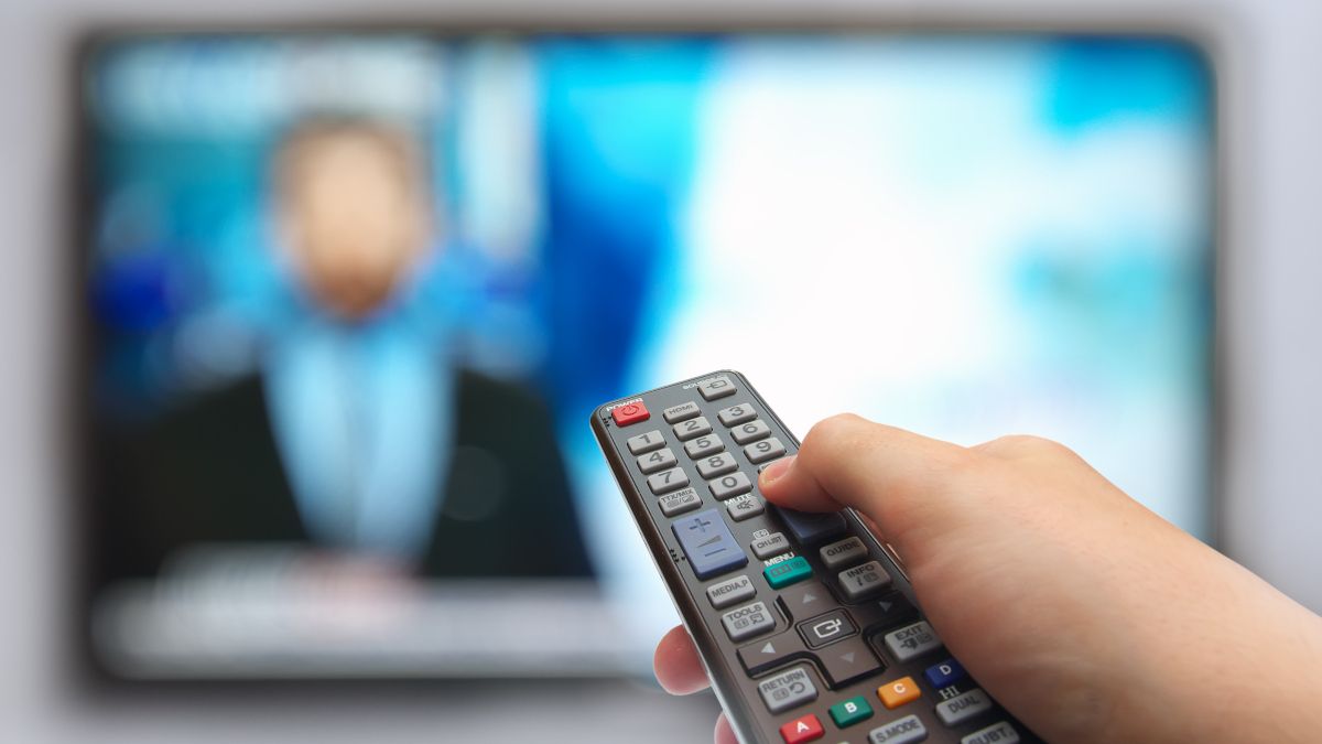 Closeup of a hand holding a remote in front of a TV screen