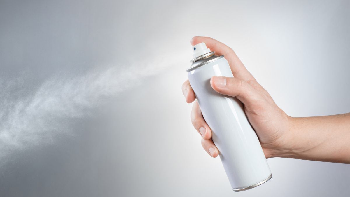Hand spraying an aerosol can over a white background.