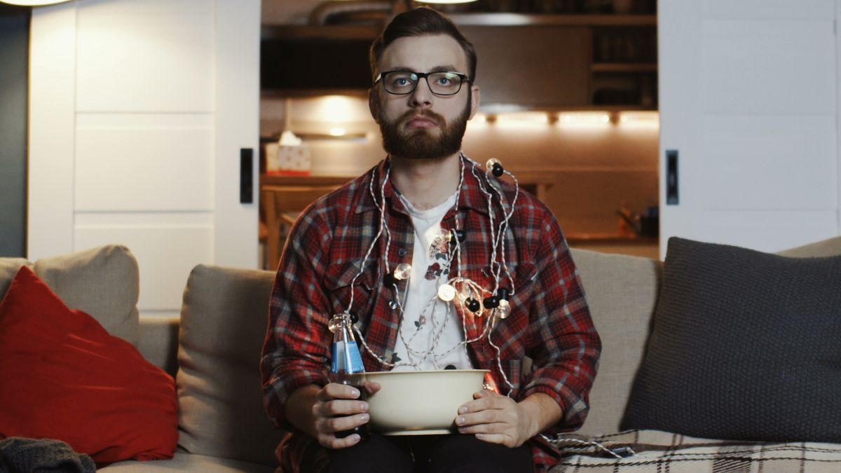 Man sitting on couch with popcorn bowl looking unimpressed.