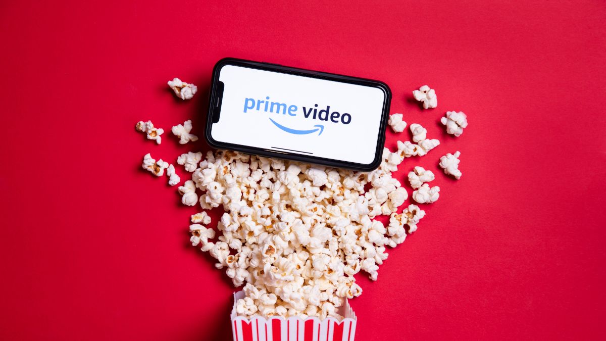 Amazon Prime Video logo on a smartphone surrounded by popcorn spilled on a red tabletop.
