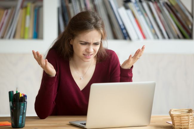 Woman looking at laptop with frustrated expression and hand in the air
