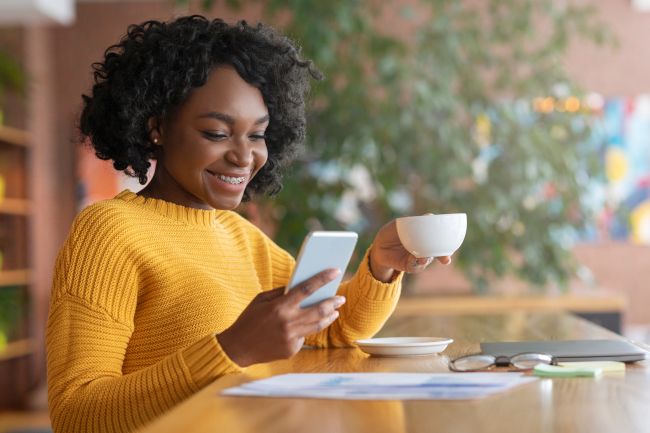 Woman drinking coffee and smiling while looking at her smartphone