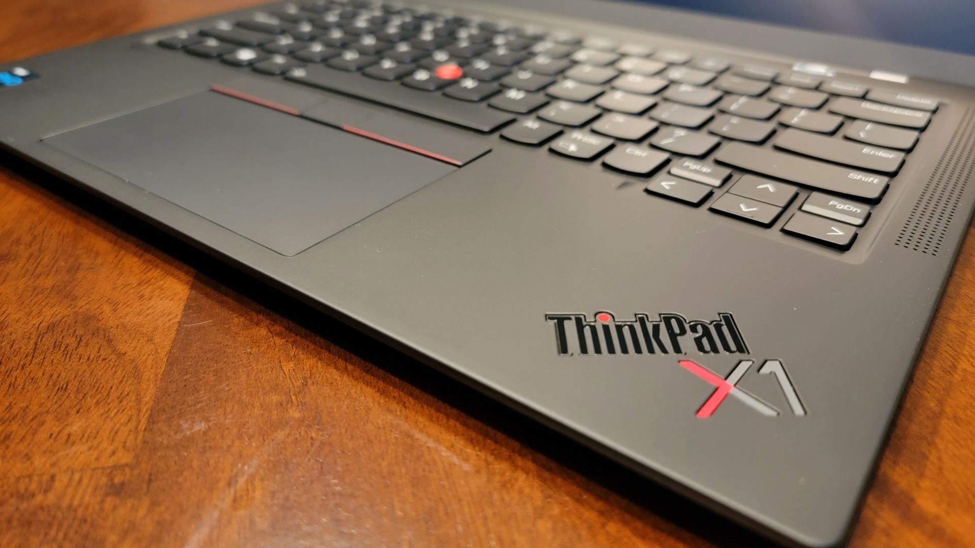 Lenovo ThinkPad X1 Carbon 9th gen laptop on a wooden table, focusing in on the Thinkpad X1 logo