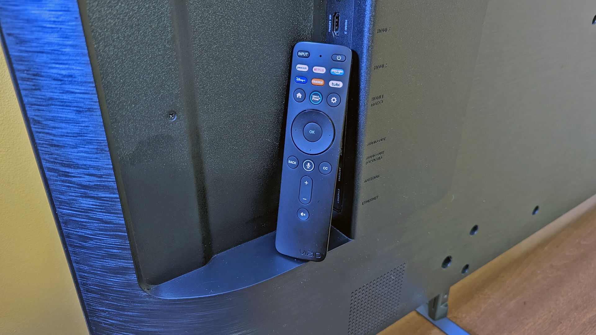 A Vizio remote against the back of a TV