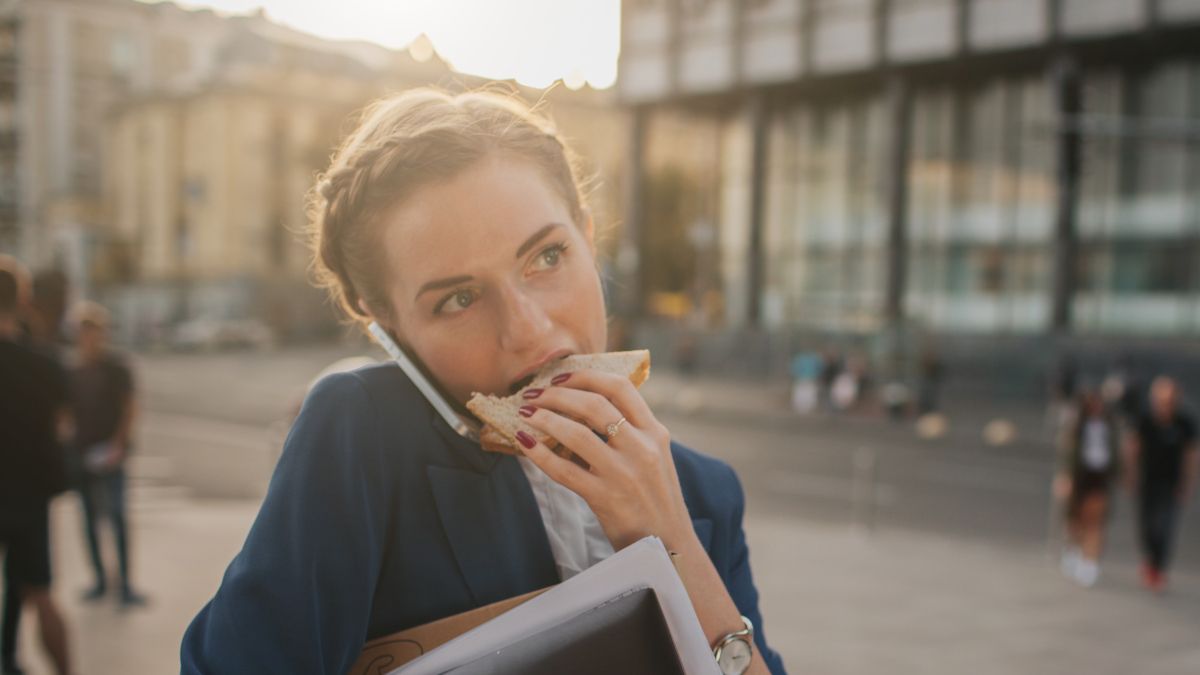Busy woman eating a sandwich and talking on a cellphone at the same time.