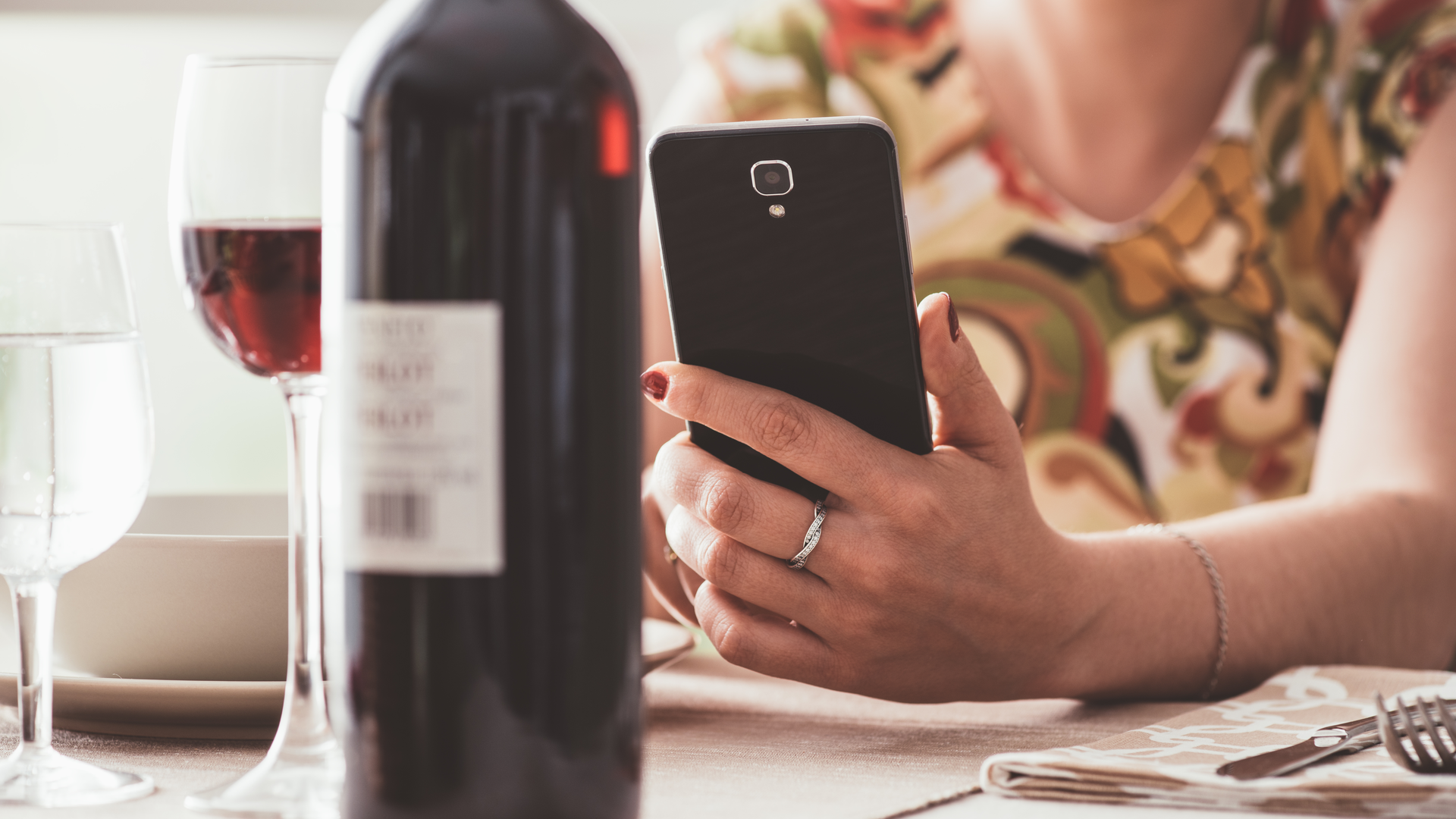 Woman having lunch at the restaurant and using a wine app with his smartphone, she is scanning the wine bottle label
