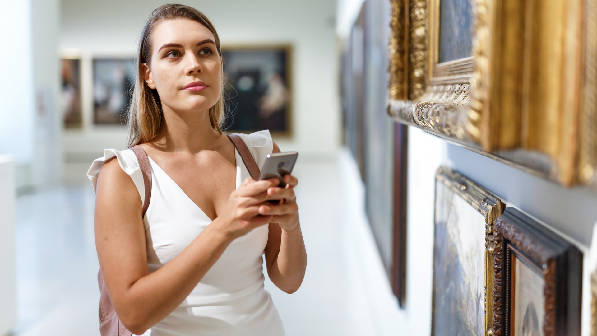 Intelligent young female using phone for search info about painting in museum