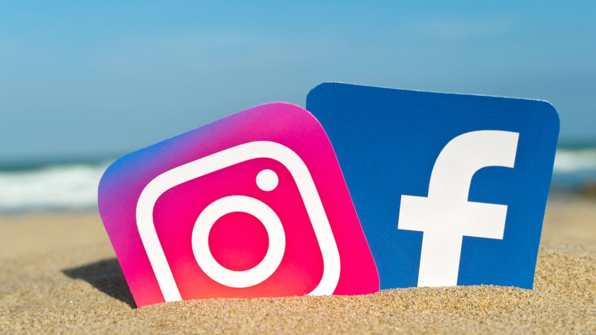 Cutouts of the Instagram and Facebook logos stuck in the sand on a sunny beach.