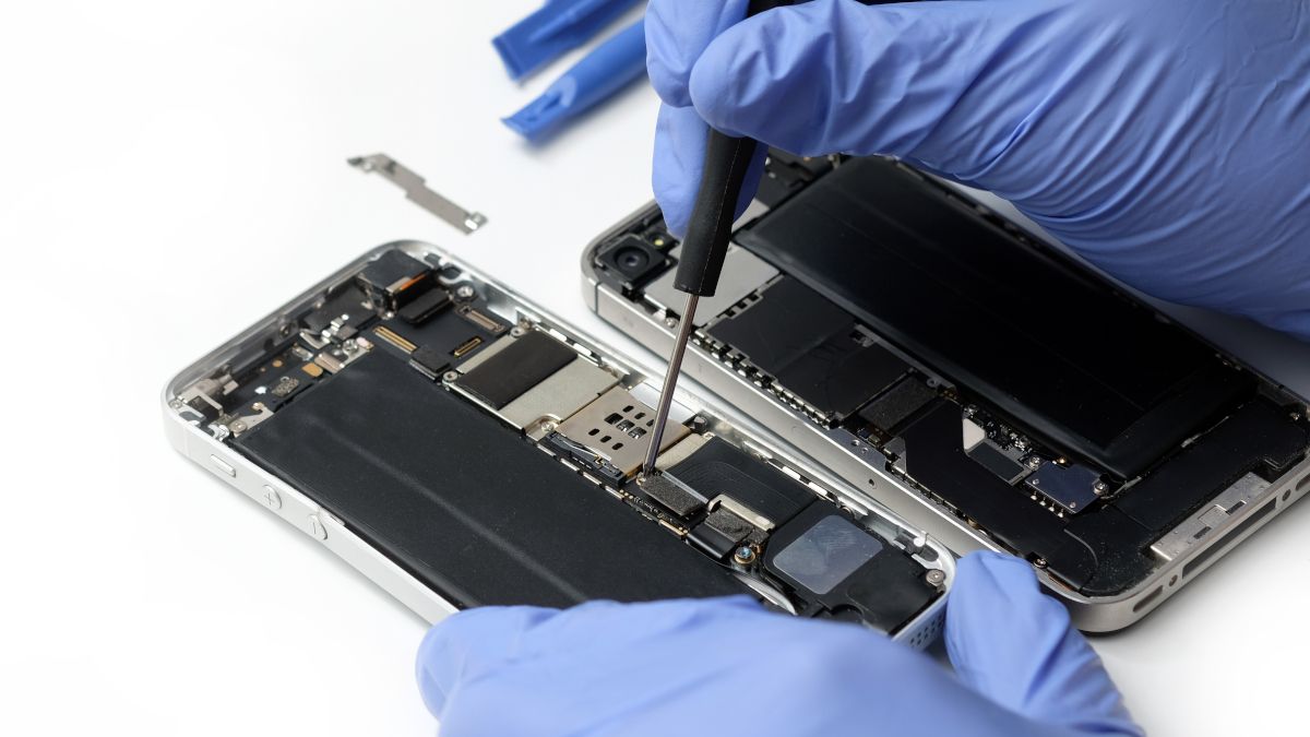 Closeup of technician's gloved hands repairing an iPhone's internal parts.