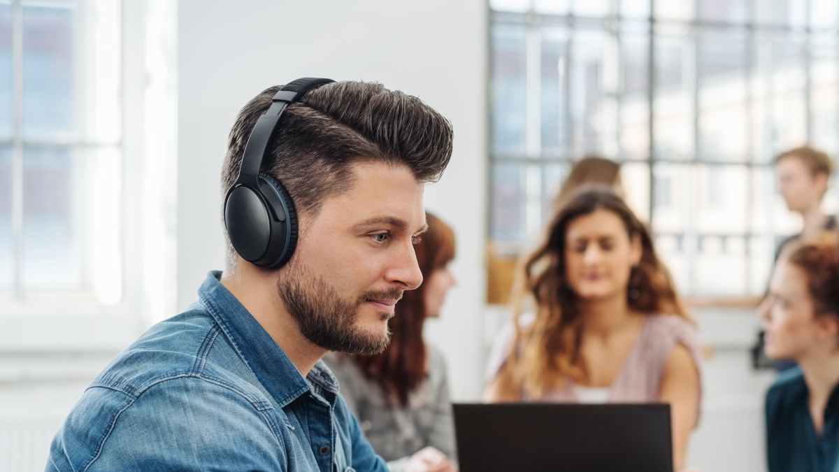 Man wearing headphones in a busy office.