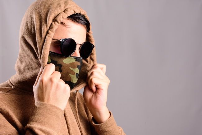 A person wearing a mask, hoodie, and sunglasses.