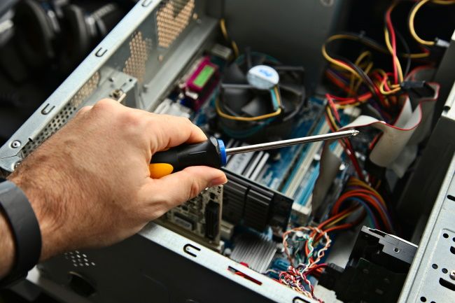 A hand holding a screwdriver above an open desktop PC case.