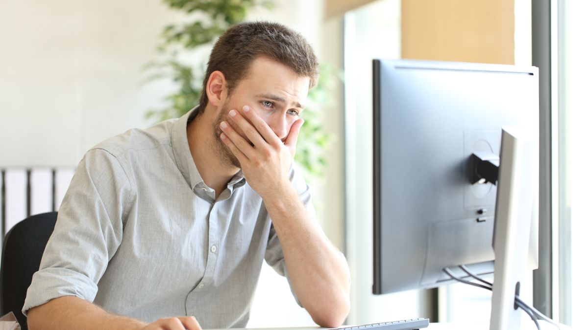Man looking at computer with shocked expression, covering mouth.