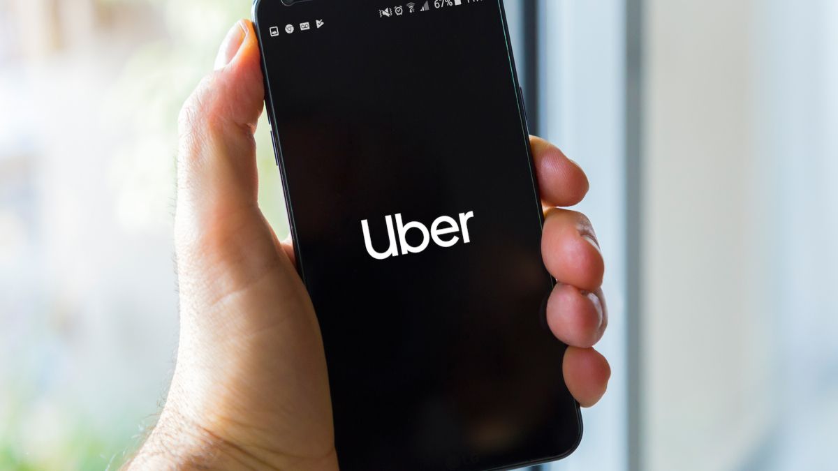 A hand holding up a smartphone displaying the Uber logo.