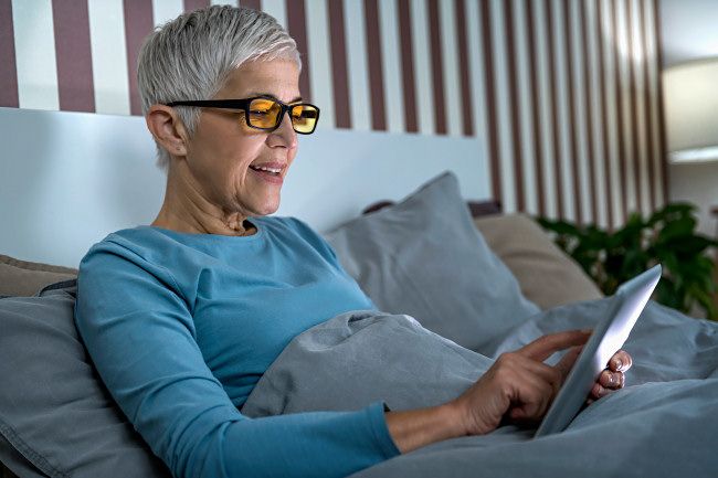 A woman using blue-light blocking glasses in bed.
