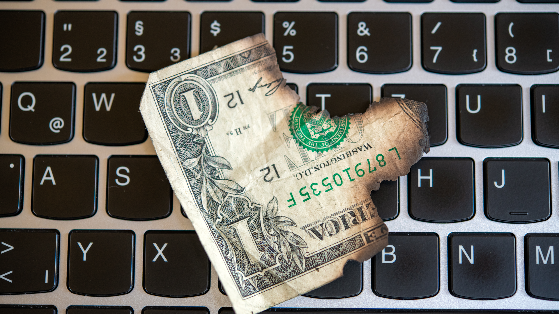 A laptop with a burnt dollar bill on the keyboard