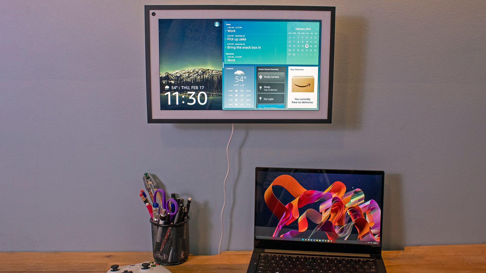 An Echo Show 15 hanging on the wall above a laptop