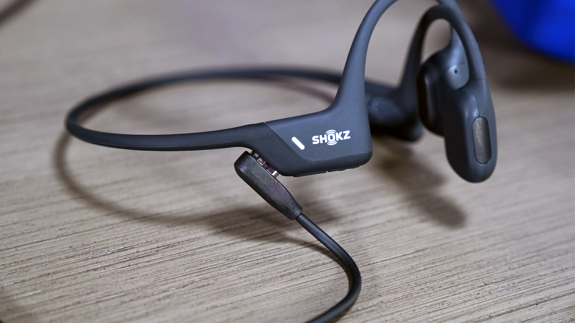 The Shokz OpenRun Pro bone conduction headphones plugged in and charging via the included proprietary charging cord.