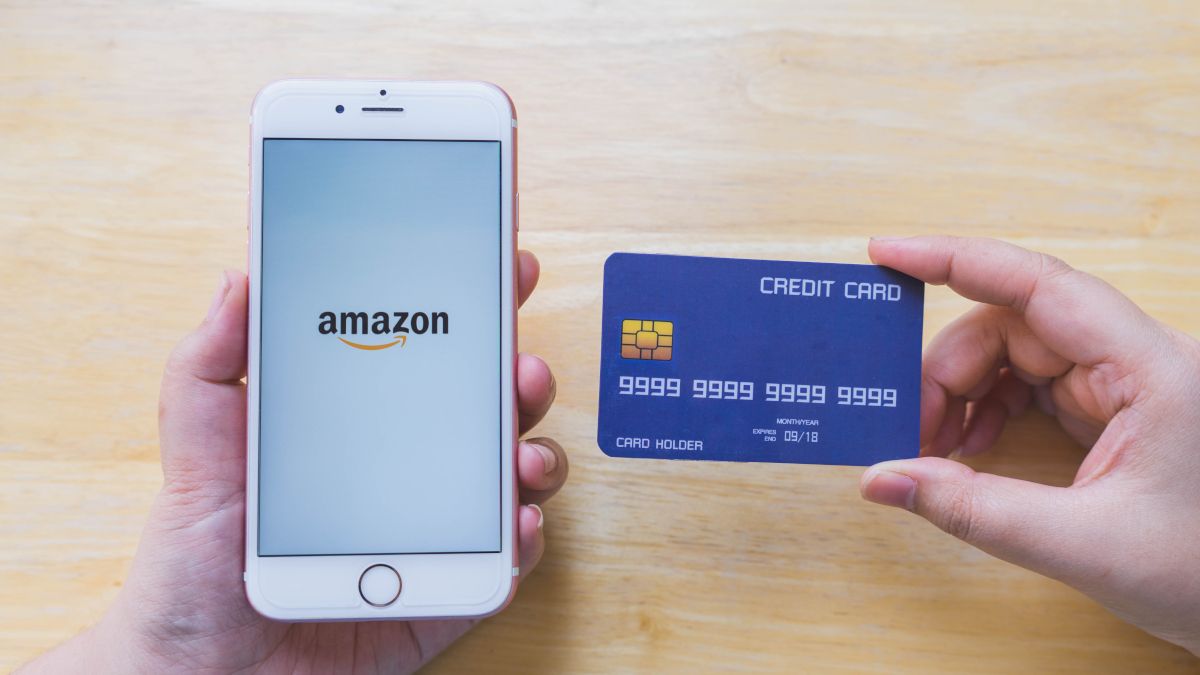 A person's hands holding a credit card and a smartphone showing the Amazon logo.