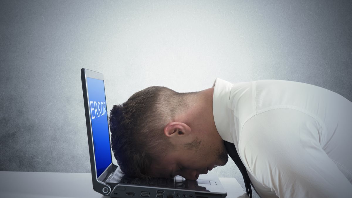 A man resting his head on a laptop with an error