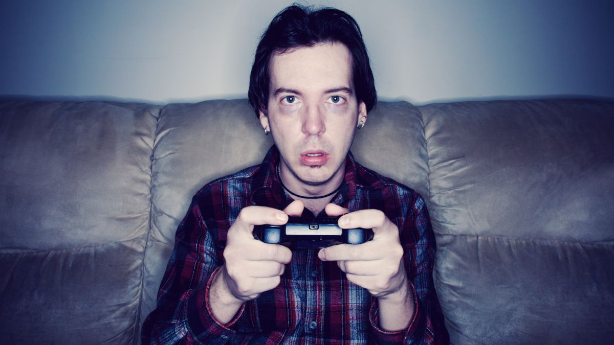 Man sitting on a couch and playing video games with an exhausted or dazed expression.