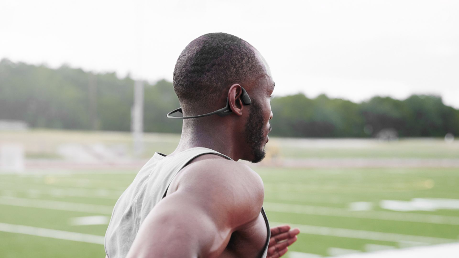 Athlete wearing the Shokz OpenRun Pro bone conducting headphones while running around an outdoor track