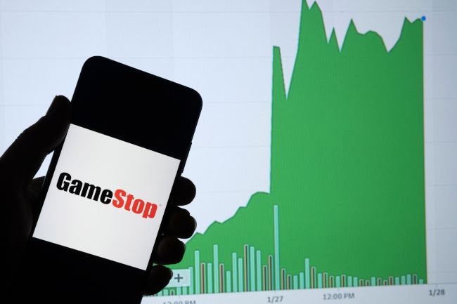 A smartphone showing the GameStop logo in front of a chart of increasing stock value.