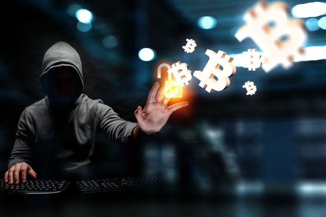 A hooded hacker figure drawing Bitcoin symbols with their hand.