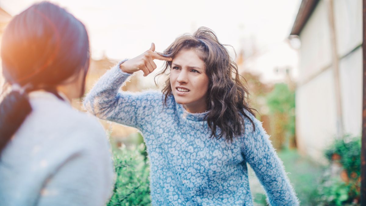 Two women arguing, with one pointing at forehead.