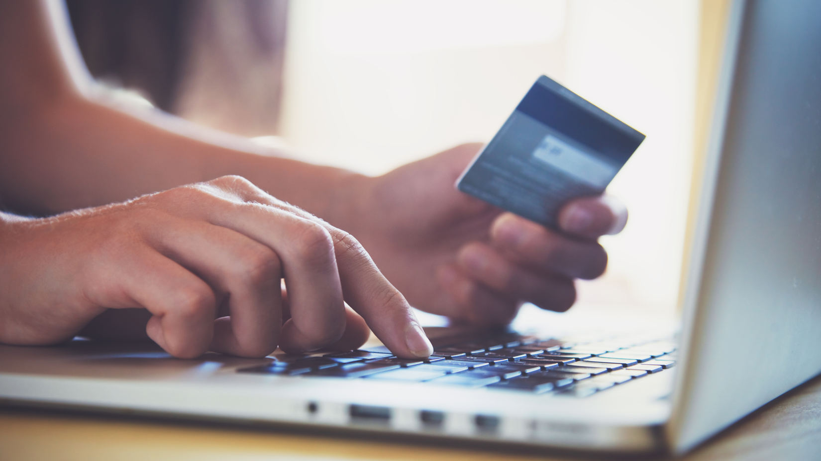 Hands holding credit card and using laptop to shop online.