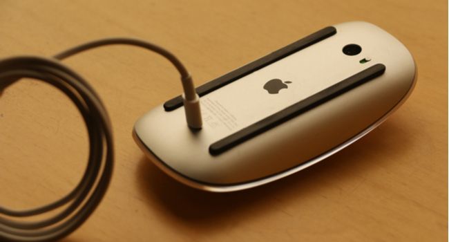 An upside-down Apple mouse with the charging cable attached.
