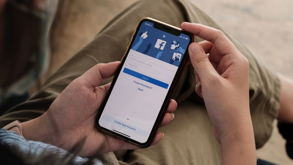 Person holding an iPhone with the Facebook app login screen visible.