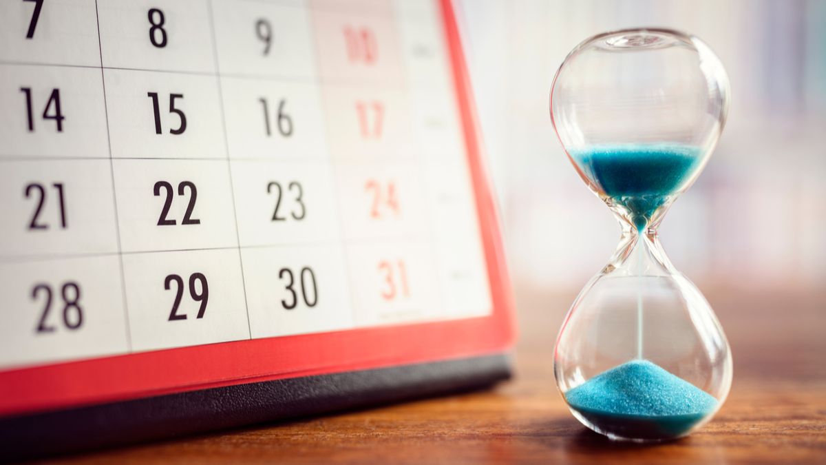 An hourglass on a tabletop next to a calendar.